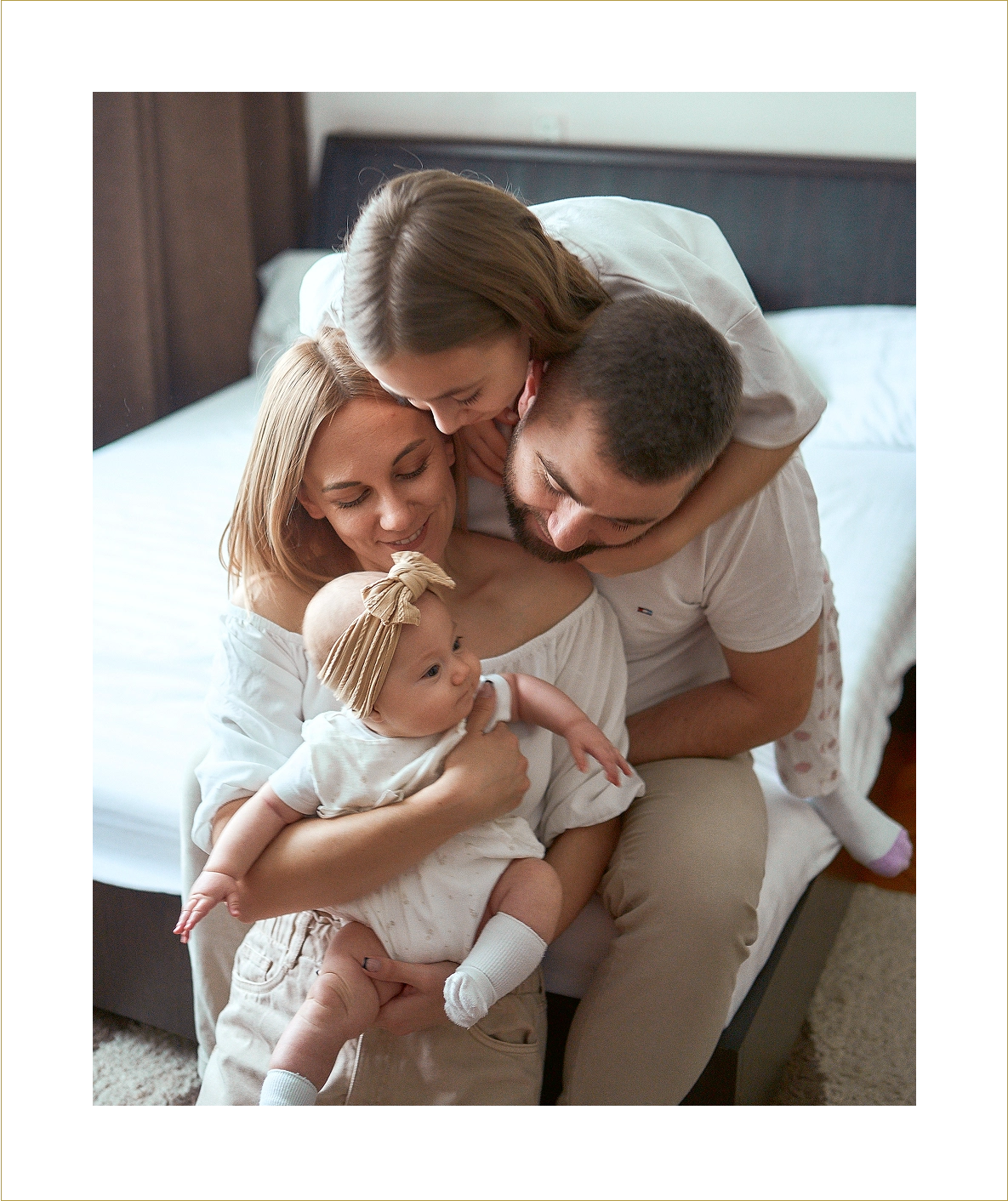 Family cuddling with baby on bed.