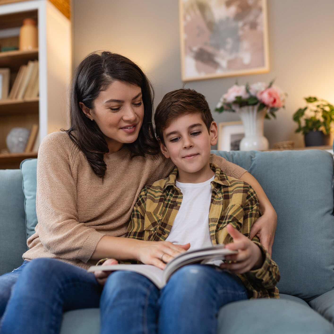Loving young mother reading book to adorable little son, sitting on cozy sofa in living room, mum teaching boy child, family spending weekend at home together, children education